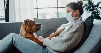 woman wearing mask sitting with a dog
