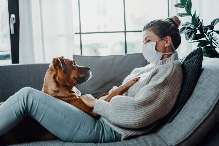 woman wearing mask sitting with a dog