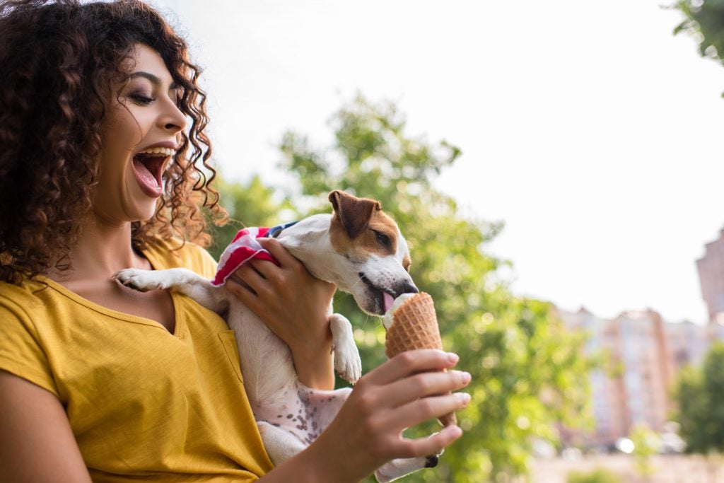 Woman holding a small dog and feeding it ice cream.