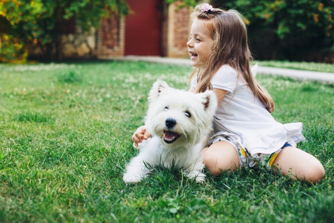 Little girl playing outside with a small white dog