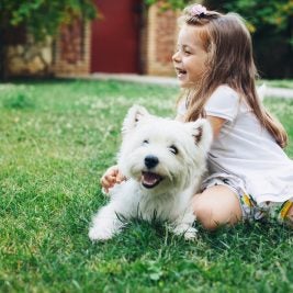 Little girl playing outside with a small white dog